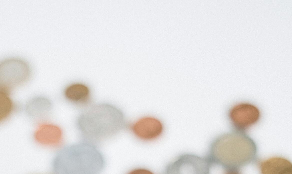 A hand holding a variety of coins with more scattered on a white surface, symbolizing currency and finance.